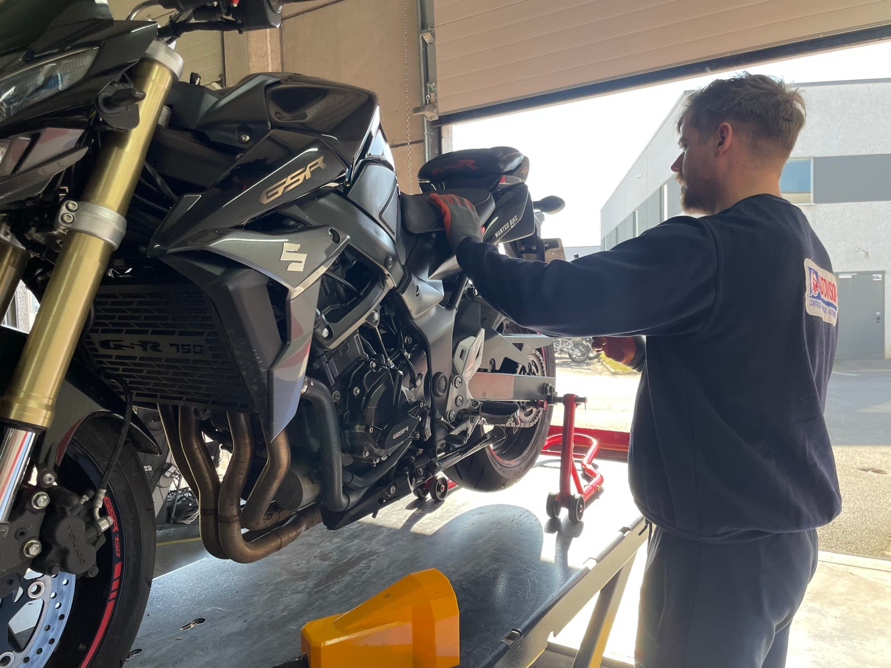 Un contrôleur agréé inspecte une moto surélevée sur la piste de contrôle technique